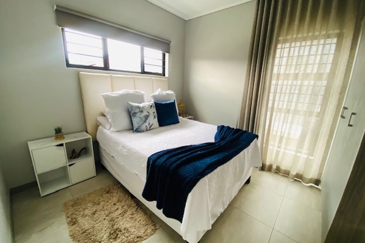 A well-maintained bedroom featuring neutral tiled flooring, a built-in wardrobe, and large windows with fitted blinds and curtains.