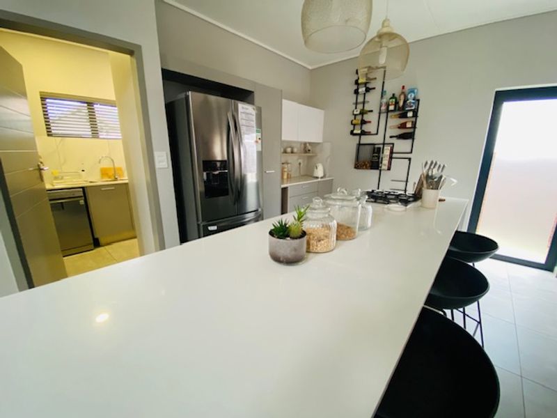 Modern kitchen featuring a large central island with quartz countertops, sleek cabinetry, and an adjacent scullery area with additional sink and storage.