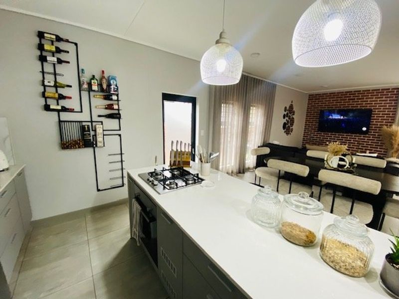 Modern open-plan kitchen and living area featuring a central island with gas hob, sleek cabinetry, and an exposed brick feature wall.