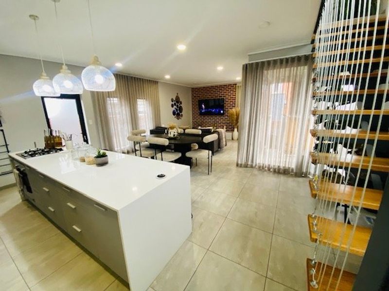 Modern open-plan living area featuring a sleek kitchen island with stone countertops, tiled floors, and a striking exposed brick feature wall.
