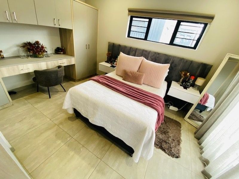 A well-maintained bedroom featuring built-in cabinetry, a dedicated desk area, tiled flooring, and a modern upholstered headboard.