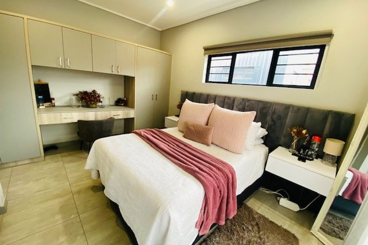 A well-maintained bedroom featuring built-in cupboards, an integrated desk area, tiled flooring, and a modern upholstered headboard.