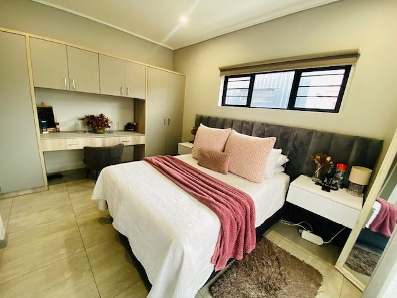 A well-maintained bedroom featuring built-in cupboards, an integrated desk area, tiled flooring, and a modern upholstered headboard.