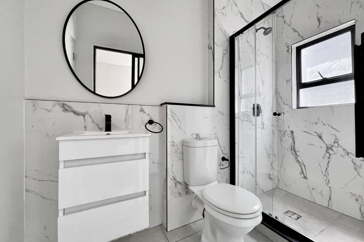 Modern bathroom featuring marble-look wall tiles, a sleek vanity cabinet, a toilet, and a walk-in shower with a black-framed glass enclosure.