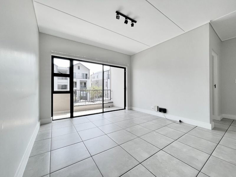 A bright, empty living room featuring neutral tiled flooring, modern track lighting, and a large sliding glass door leading to a balcony.