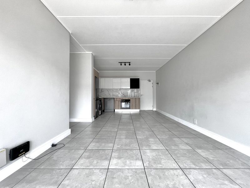 A spacious open-plan living and kitchen area featuring modern tiled flooring, contemporary cabinetry, and integrated kitchen appliances in a clean, neutral setting.