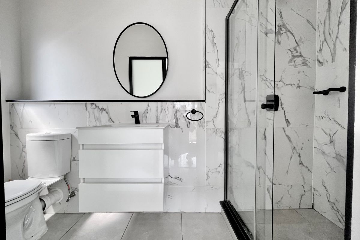 Modern bathroom featuring marble-look wall tiles, a floating vanity, black fixtures, and a glass-enclosed shower.