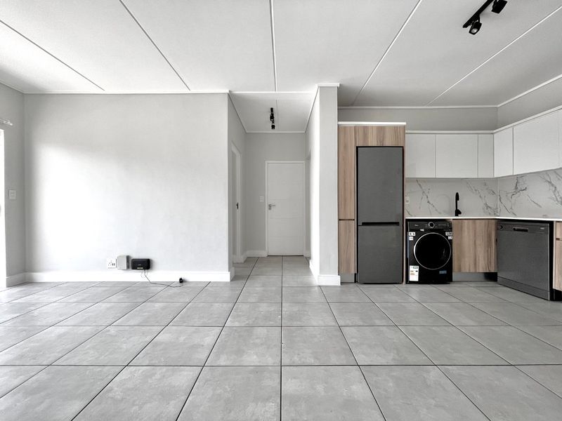 Modern open-plan living area featuring sleek tiled floors, contemporary kitchen cabinetry with marble-look backsplash, and integrated appliances in a bright, minimalist space.