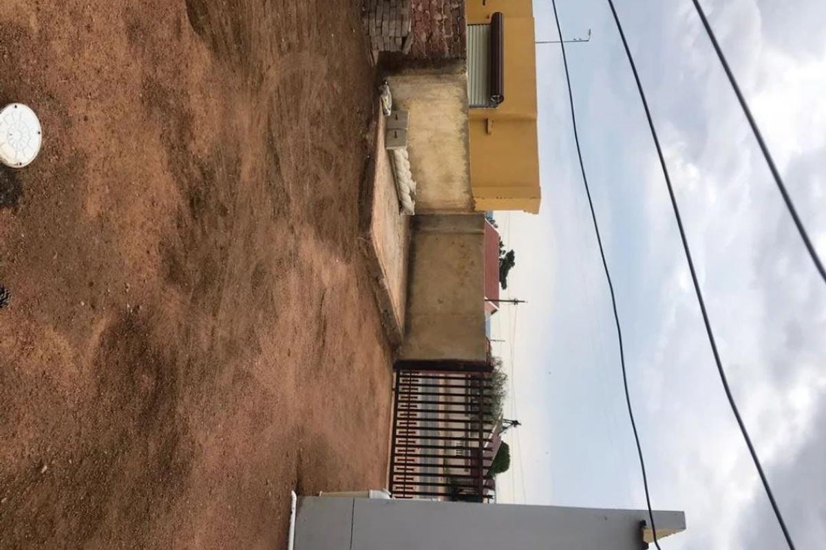 A rear outdoor area featuring a boundary wall, metal gate, and unlandscaped ground, offering potential for garden development or landscaping.