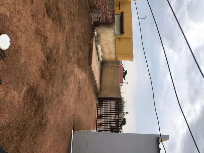 A rear outdoor area featuring a boundary wall, metal gate, and unlandscaped ground, offering potential for garden development or landscaping.