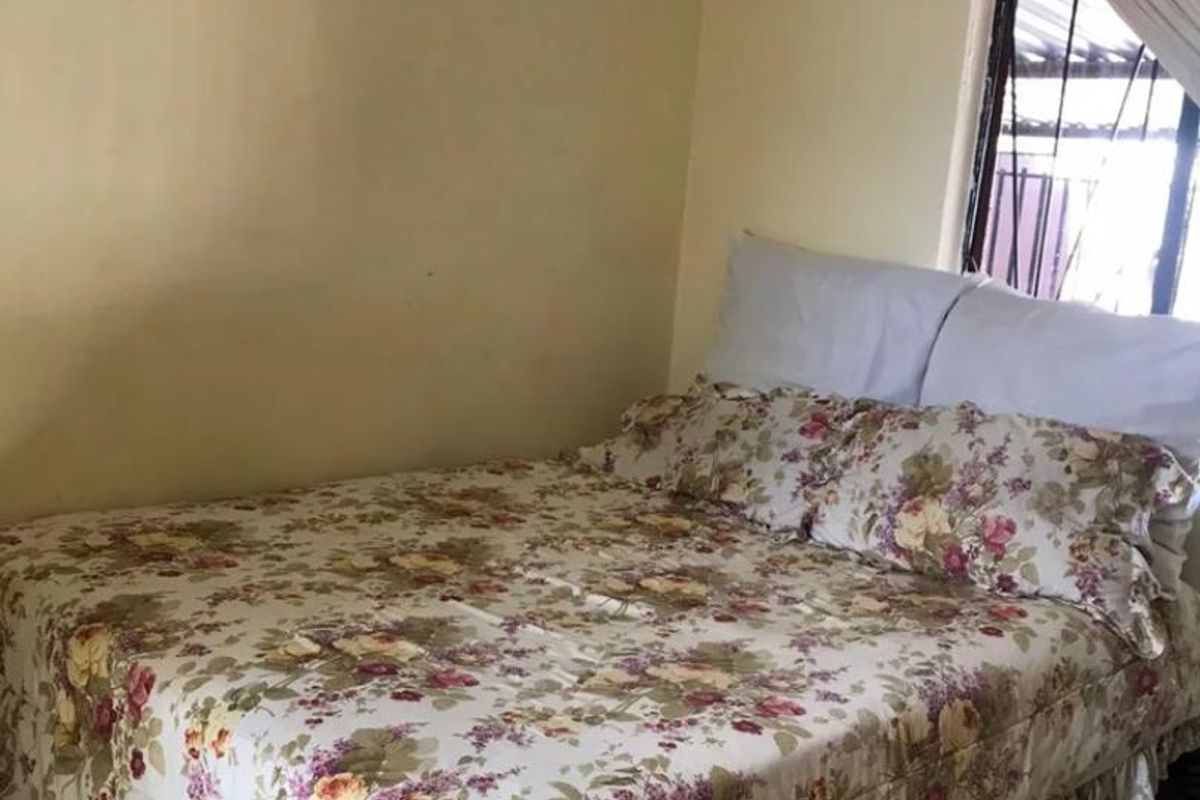 A bedroom featuring a window with security bars and coving, requiring cosmetic updates to the wall finishes.