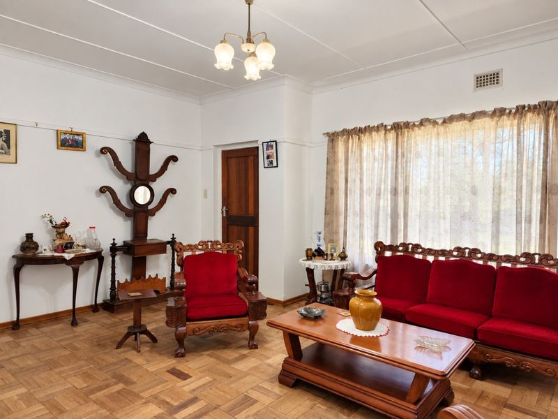 A well-maintained living room featuring classic parquet flooring, neutral walls, and a traditional ceiling light fixture.