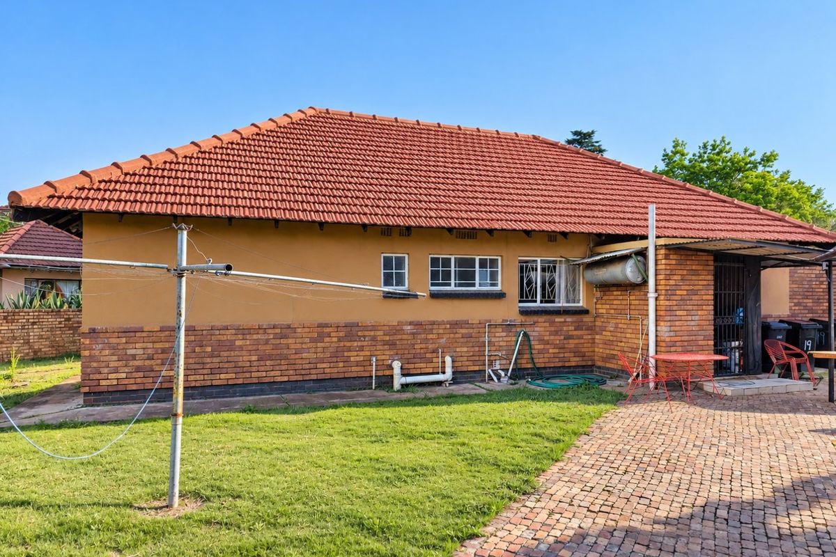 Rear view of the house featuring a terracotta tiled roof, brick facade, paved walkway, and a well-maintained lawn area.