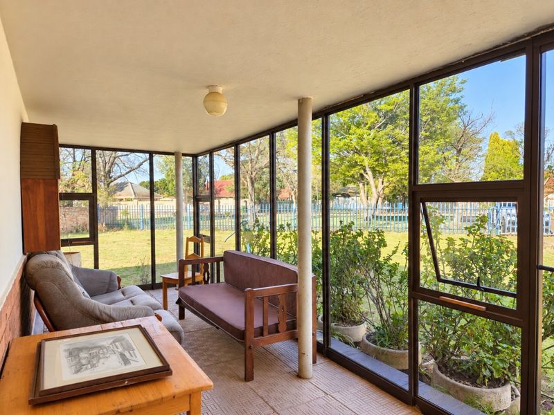 Enclosed sunroom or patio featuring large metal-framed glass windows overlooking the garden, providing a bright and versatile indoor-outdoor living space.
