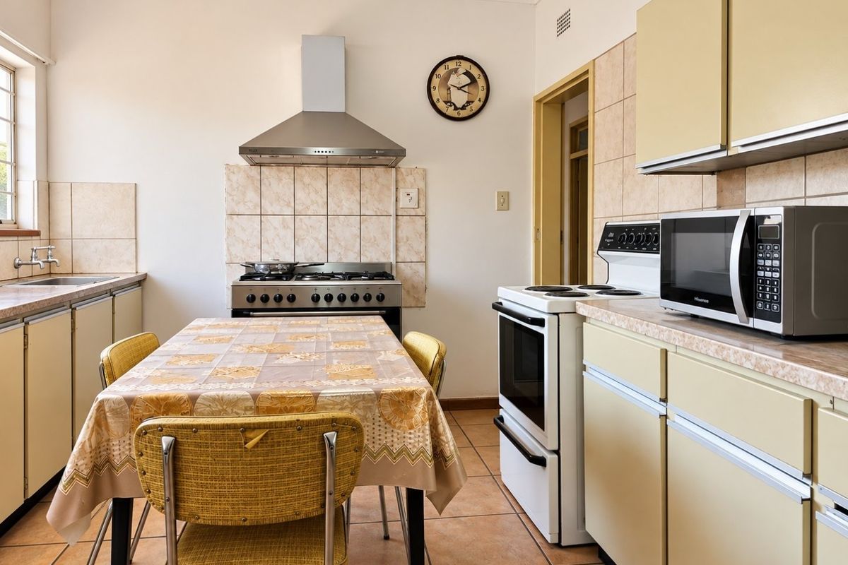 A functional kitchen featuring dual stove setups, tiled splashbacks, laminate countertops, and ample built-in cabinetry with ceramic floor tiles.