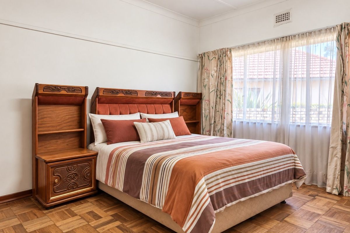 A well-maintained bedroom featuring classic parquet flooring, neutral walls, and large windows that provide ample natural light.