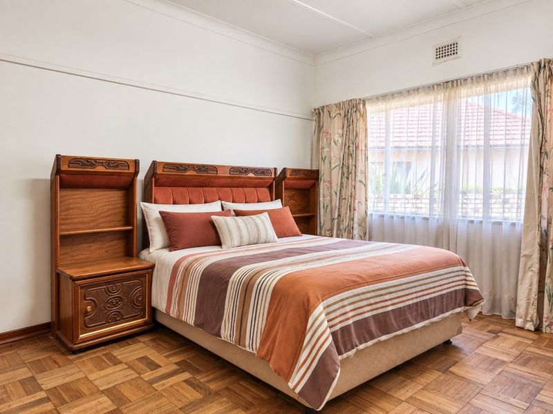 A well-maintained bedroom featuring classic parquet flooring, neutral walls, and large windows that provide ample natural light.