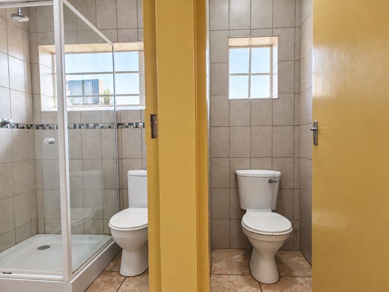 A functional bathroom featuring a separate shower enclosure and toilet with neutral wall tiling and tiled flooring.