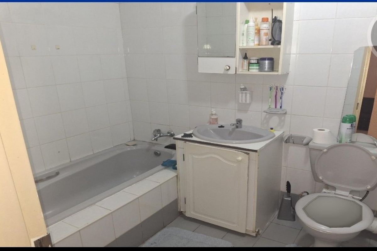 A functional bathroom featuring a bathtub, vanity cabinet with integrated basin, and toilet, finished with white wall tiles.