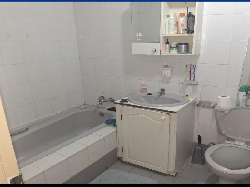 A functional bathroom featuring a bathtub, vanity cabinet with integrated basin, and toilet, finished with white wall tiles.