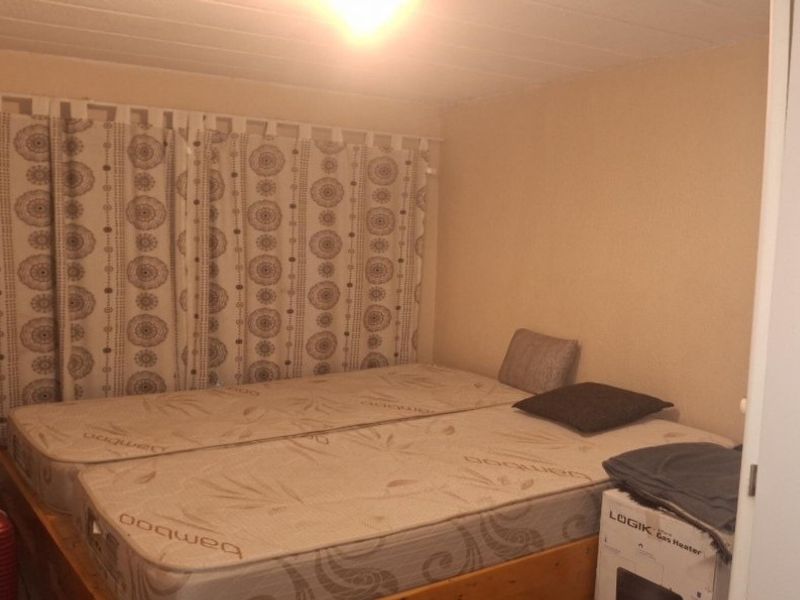 A bedroom featuring a timber ceiling and curtain tracks, currently used as a sleeping area.