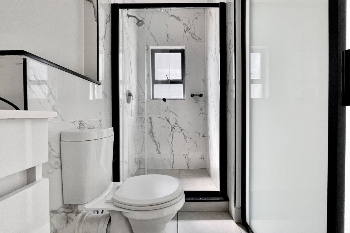 Modern bathroom featuring a walk-in shower with black-framed glass enclosure and elegant marble-look wall tiles.