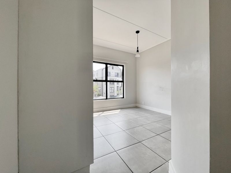 A bright, empty bedroom featuring neutral tiled flooring, a modern black-framed window, and a simple pendant light fixture.