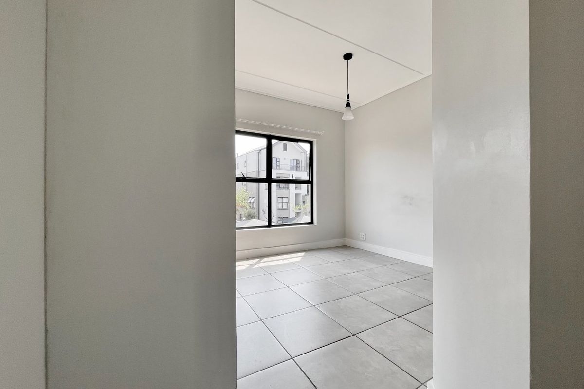 A bright, empty bedroom featuring neutral tiled flooring, a modern black-framed window, and a simple pendant light fixture.