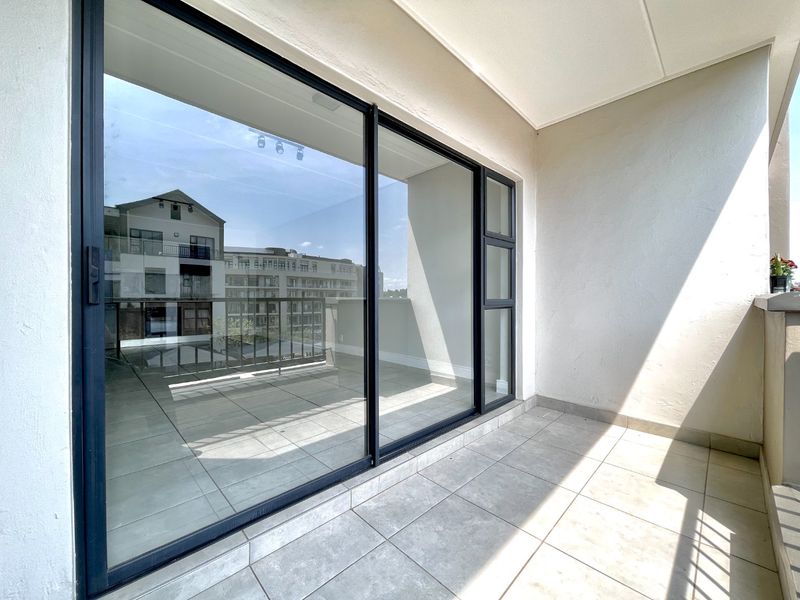 A clean, tiled balcony featuring large sliding glass doors and modern aluminum frames, offering a bright and functional outdoor space.