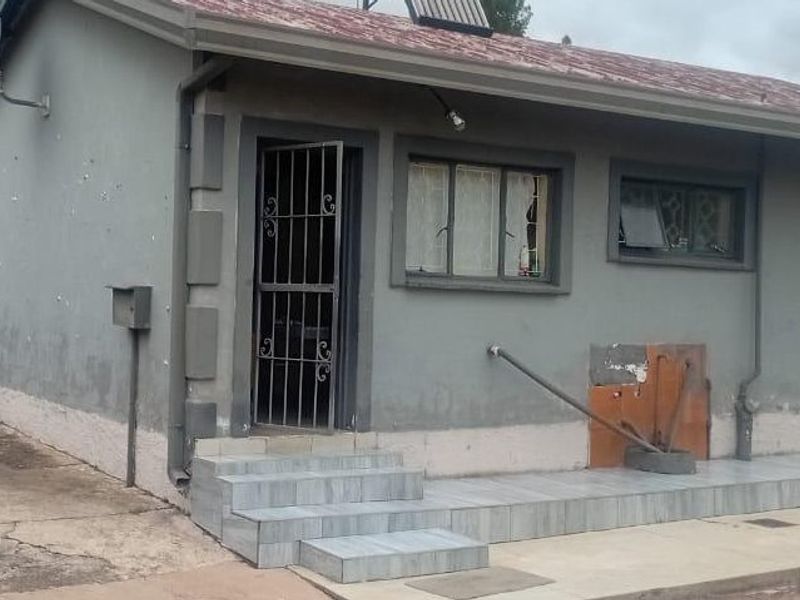Front exterior view of a single-story house featuring a tiled porch, security gate, and solar water heater, showing signs of wear on the exterior walls.
