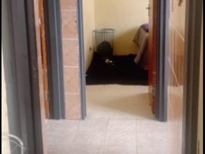 A narrow hallway featuring tiled flooring and tiled wall cladding, providing access to adjacent rooms.
