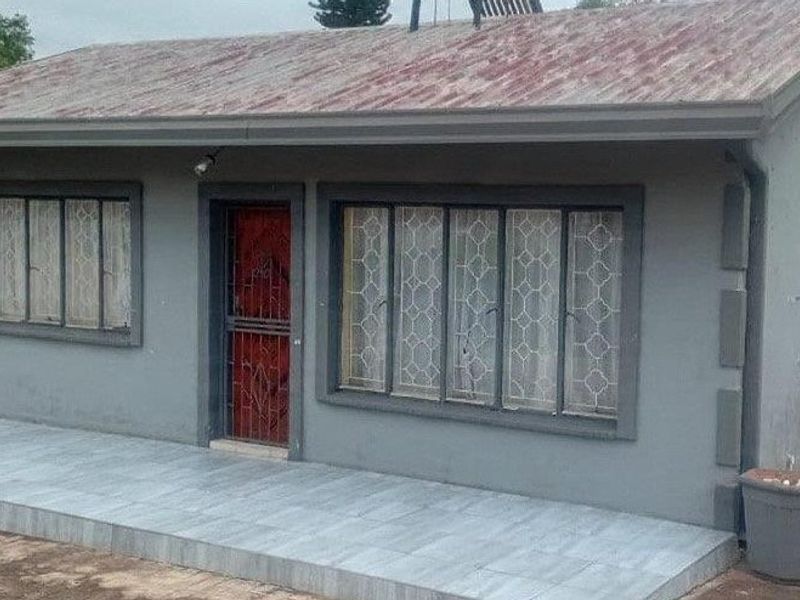 Front elevation of a single-story house featuring a tiled porch, security gate, and metal-framed windows under a tiled roof.