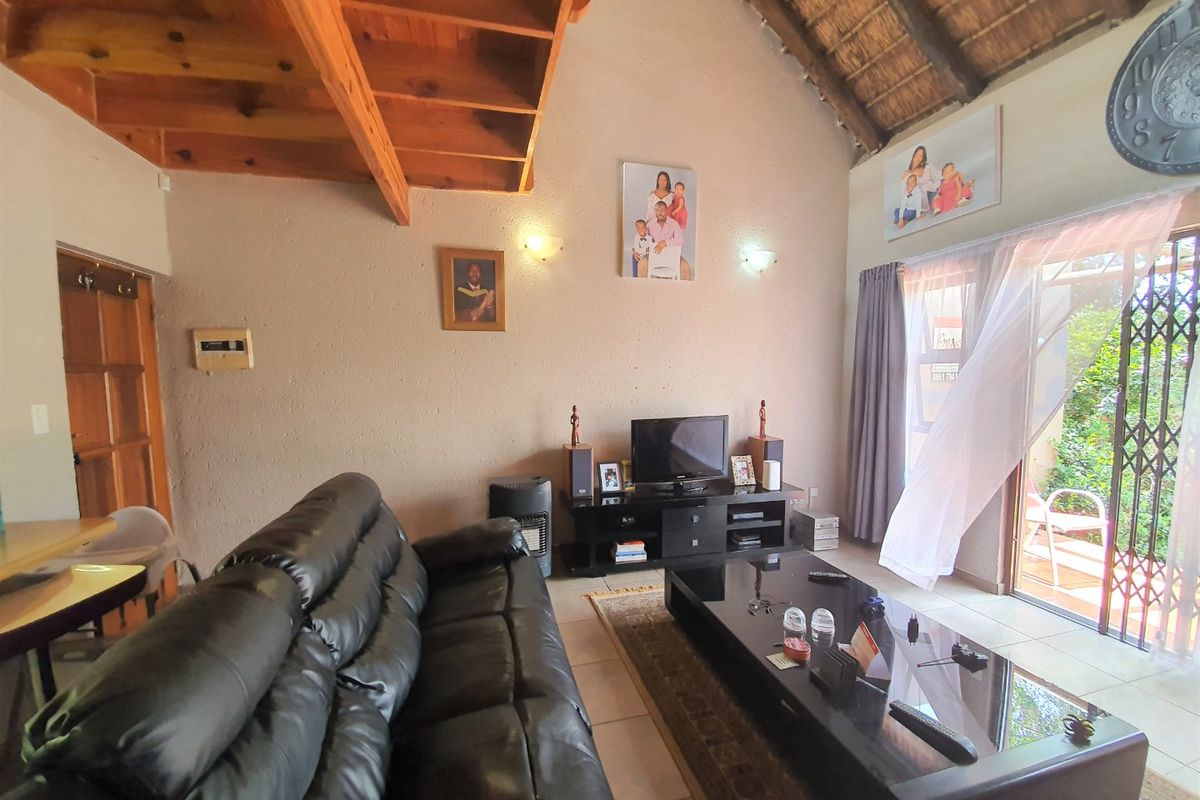 Spacious living room featuring a high-pitched thatched roof with exposed timber beams, tiled flooring, and direct access to an outdoor patio area.