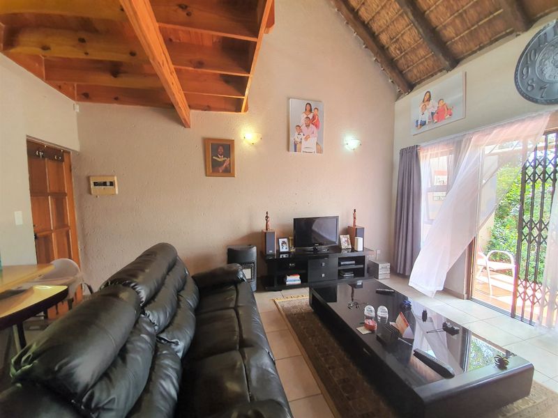 Spacious living room featuring a high-pitched thatched roof with exposed timber beams, tiled flooring, and direct access to an outdoor patio area.