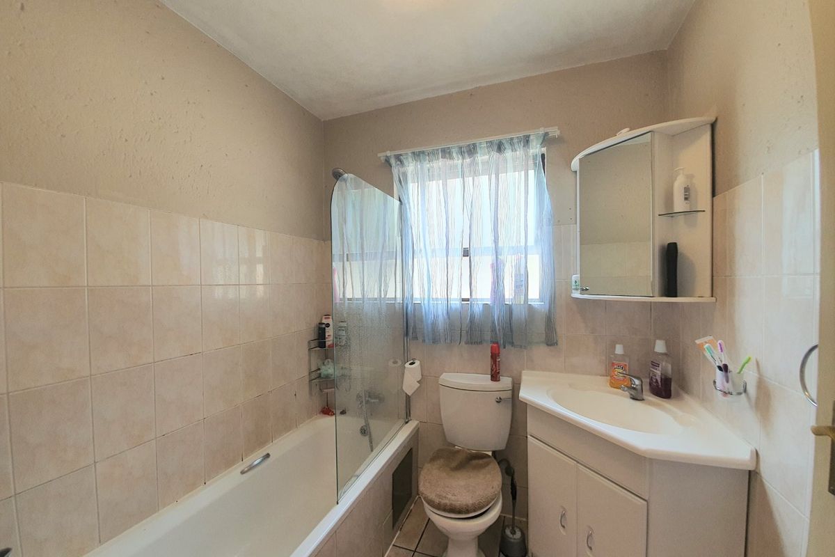 A functional bathroom featuring a bathtub with a glass screen, a vanity unit with a basin, and a toilet, finished with neutral wall tiles.