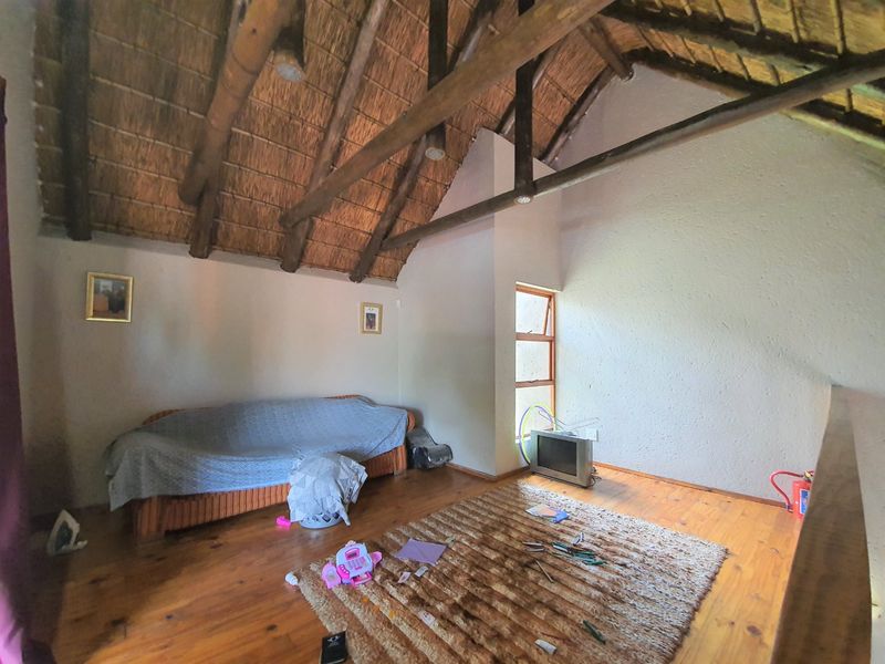 A bedroom featuring a high-pitched thatched ceiling with exposed timber rafters and warm timber flooring, offering a rustic and spacious atmosphere.