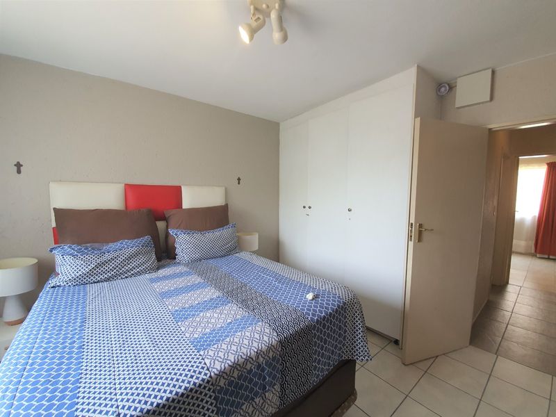 A functional bedroom featuring built-in cupboards, tiled flooring, and a ceiling-mounted spotlight fixture.