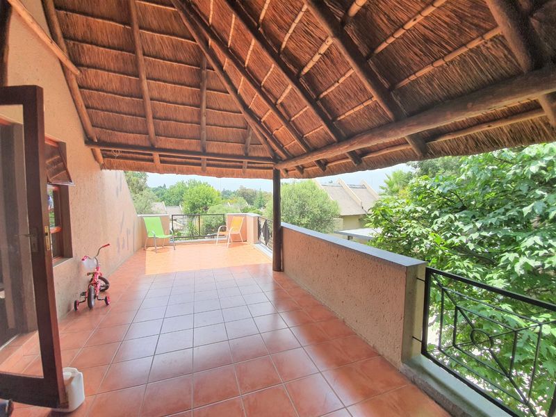 A spacious covered balcony featuring a traditional thatched roof, tiled flooring, and wrought iron railings, offering an open-air space for outdoor relaxation.
