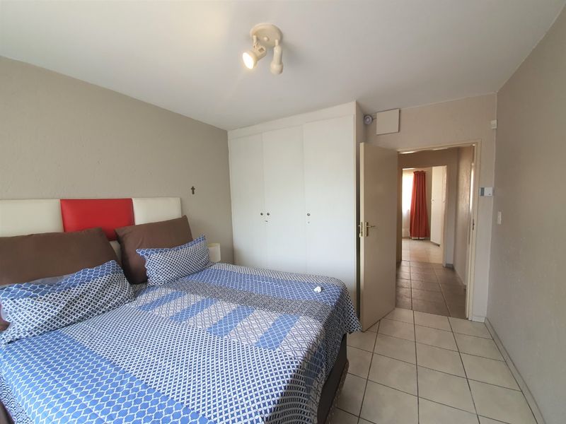 A functional bedroom featuring tiled flooring, built-in cupboards, and a ceiling-mounted spotlight fixture, with direct access to an adjoining hallway.