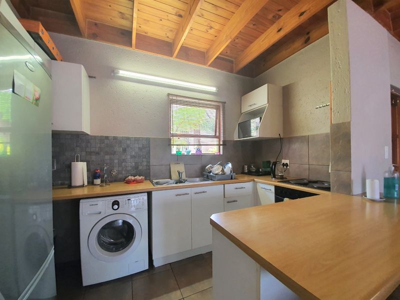Functional kitchen featuring exposed timber beam ceilings, laminate countertops, built-in cabinetry, and integrated appliances with a tiled backsplash and floor.