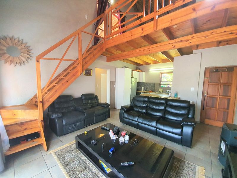 Open plan living area featuring a timber staircase leading to a mezzanine level, tiled flooring, and an integrated kitchen space.