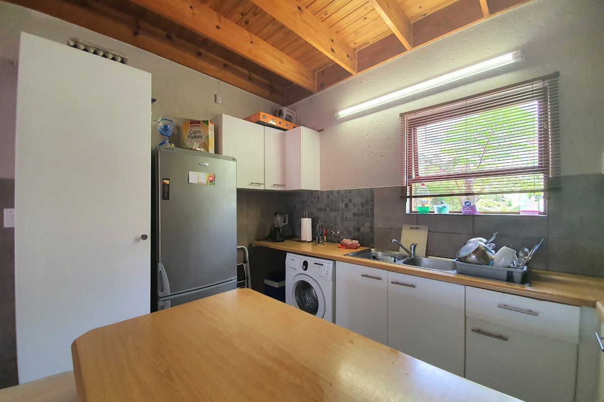 A functional kitchen featuring exposed timber beam ceilings, laminate countertops, a double basin sink, and built-in cabinetry with a tiled backsplash.