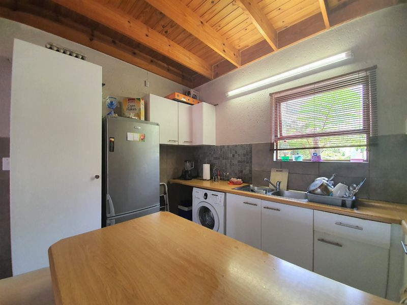 A functional kitchen featuring exposed timber beam ceilings, laminate countertops, a double basin sink, and built-in cabinetry with a tiled backsplash.