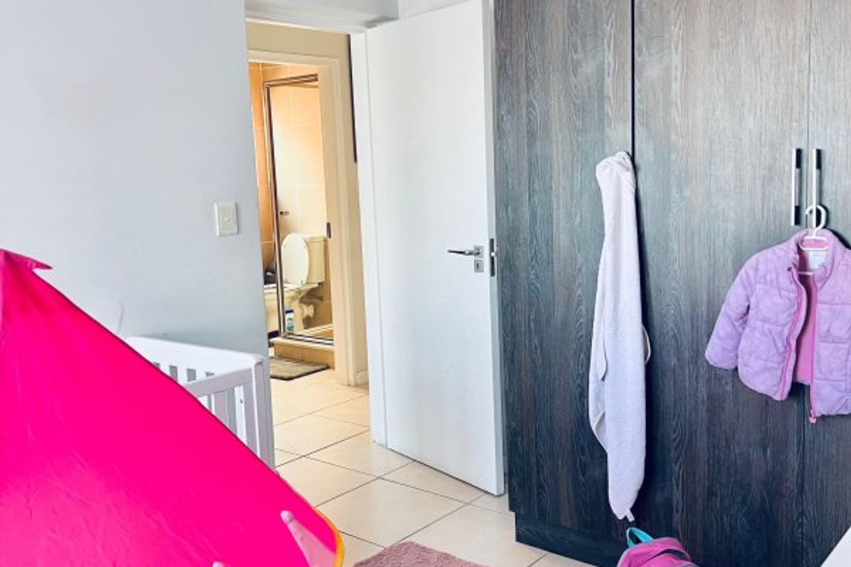 A bedroom featuring dark wood-finish built-in cupboards, tiled flooring, and direct access to an en-suite bathroom.