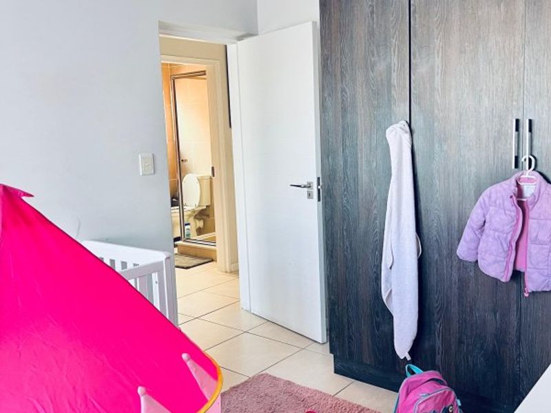 A bedroom featuring dark wood-finish built-in cupboards, tiled flooring, and direct access to an en-suite bathroom.