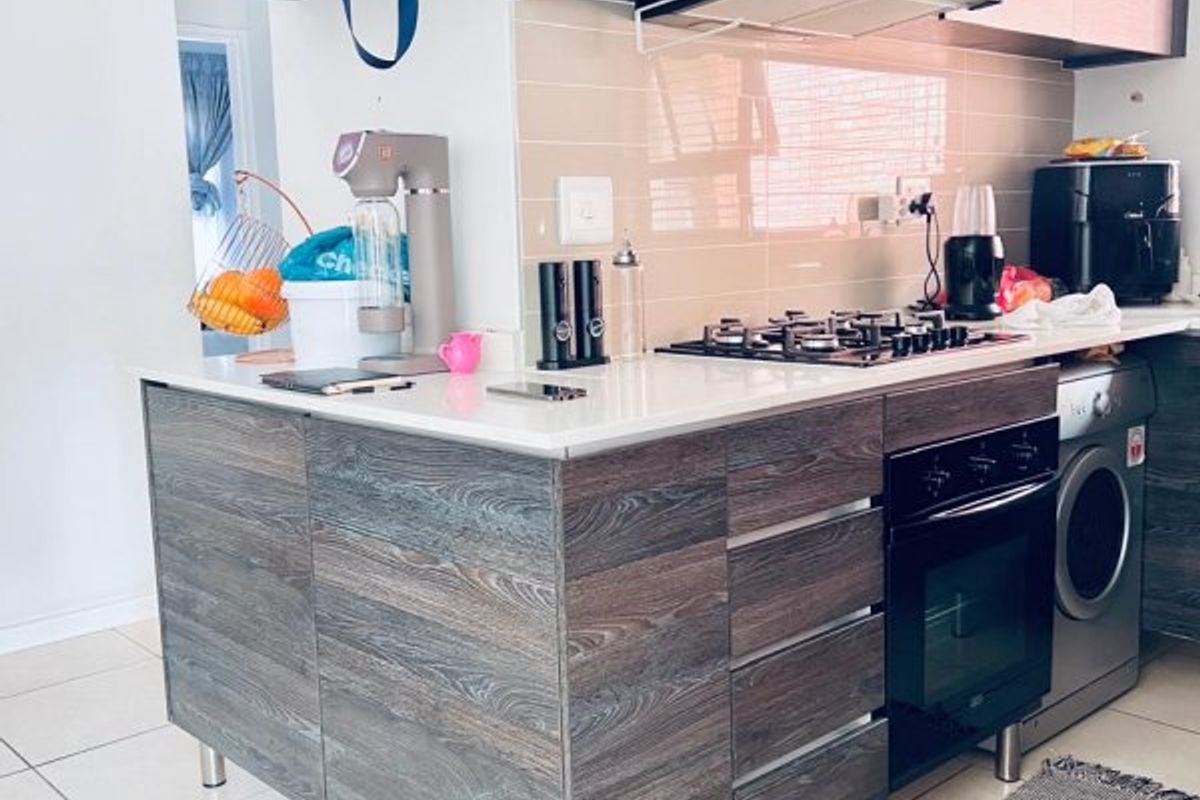 Modern kitchen featuring dark wood-grain cabinetry, stone countertops, a gas hob, built-in oven, and integrated laundry appliance with neutral tiled flooring.