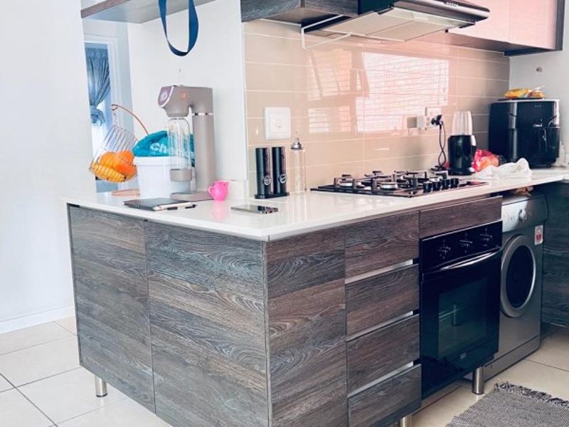 Modern kitchen featuring dark wood-grain cabinetry, stone countertops, a gas hob, built-in oven, and integrated laundry appliance with neutral tiled flooring.