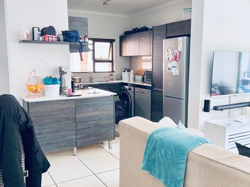 Open plan living area featuring a compact kitchen with built-in cabinetry, tiled flooring, and integrated appliances, seamlessly flowing into the living space.