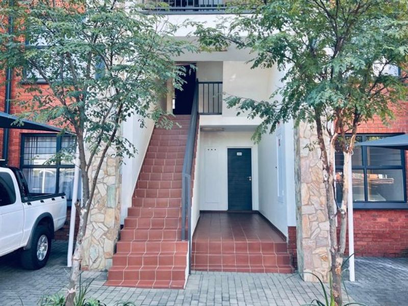 Front exterior view of an apartment building featuring a brick and stone facade, tiled staircase, and paved entrance walkway.
