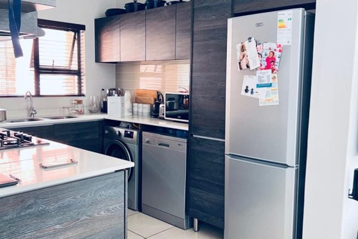 Modern kitchen featuring dark wood-grain cabinetry, stone countertops, tiled flooring, and integrated appliances including a dishwasher and hob.